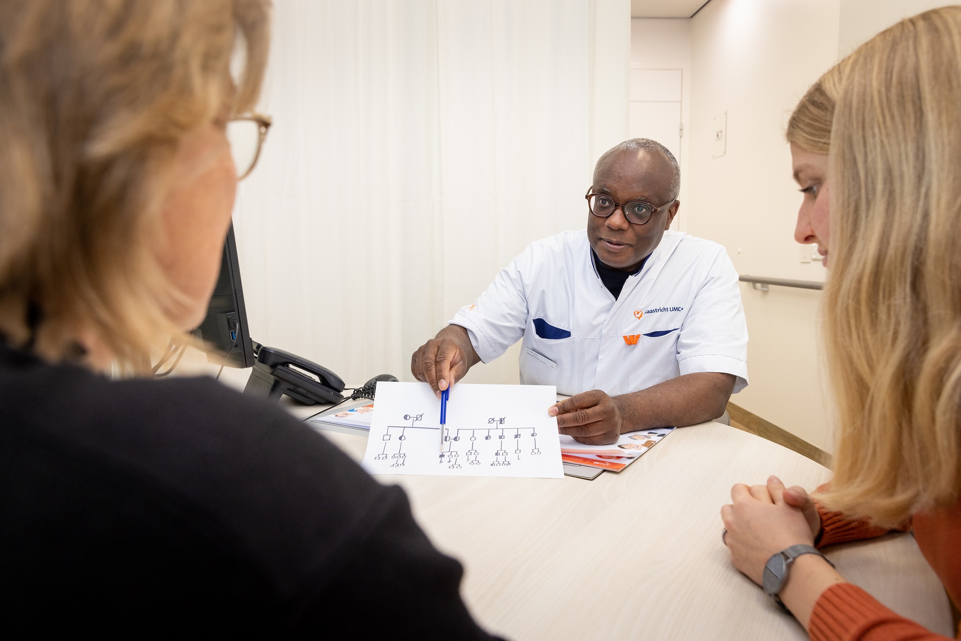 De klinisch geneticus legt een moeder en haar dochter hun stamboomtekening uit