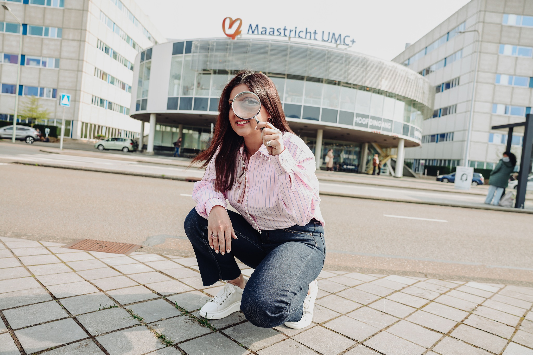 Athina Vidaki met een vergrootglas gehurkt zittend voor het Maastricht UMC+