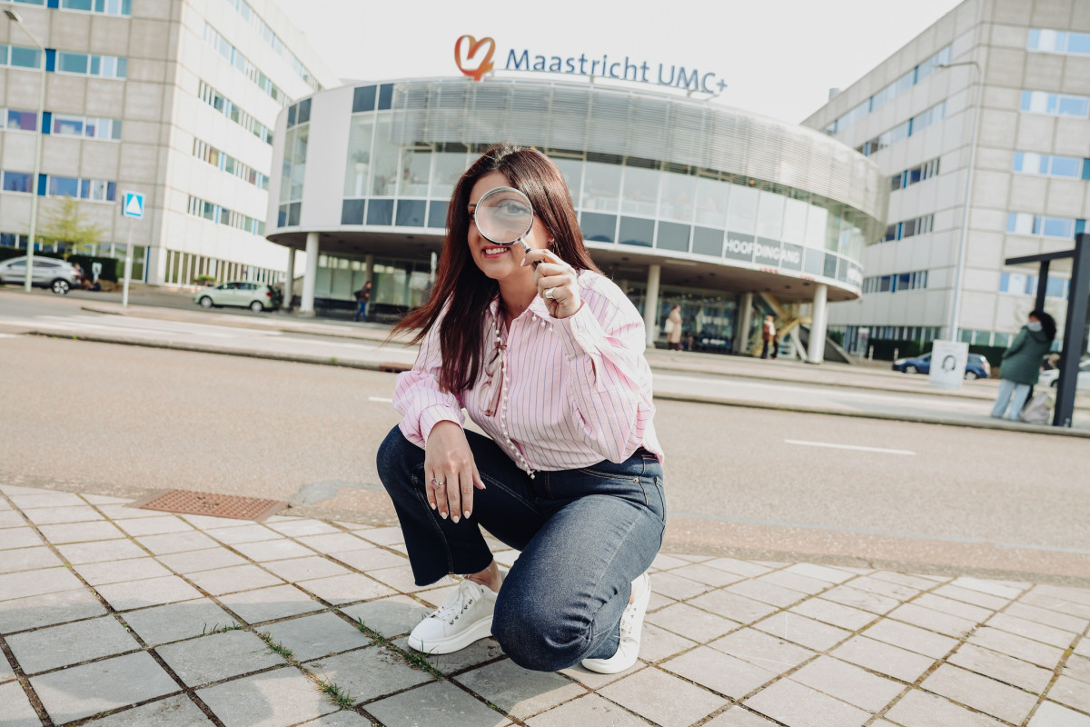 Athina Vidaki met een vergrootglas gehurkt zittend voor het Maastricht UMC+